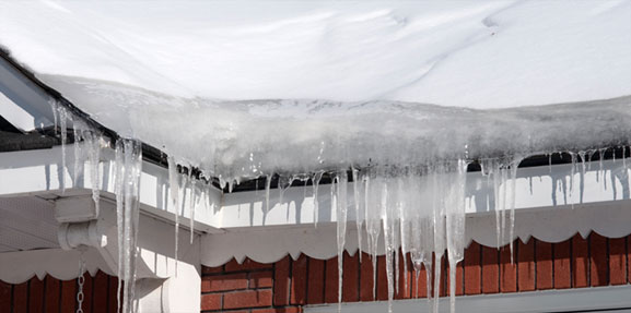 Icicles forming an ice dam on the roof of a house in the Winter.