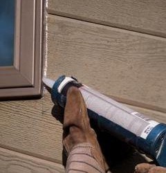 Person putting new silicone caulking on exteriors of window frames as part of their Springtime home maintenance.