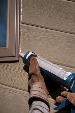Person putting new silicone caulking on exteriors of window frames as part of their Springtime home maintenance.